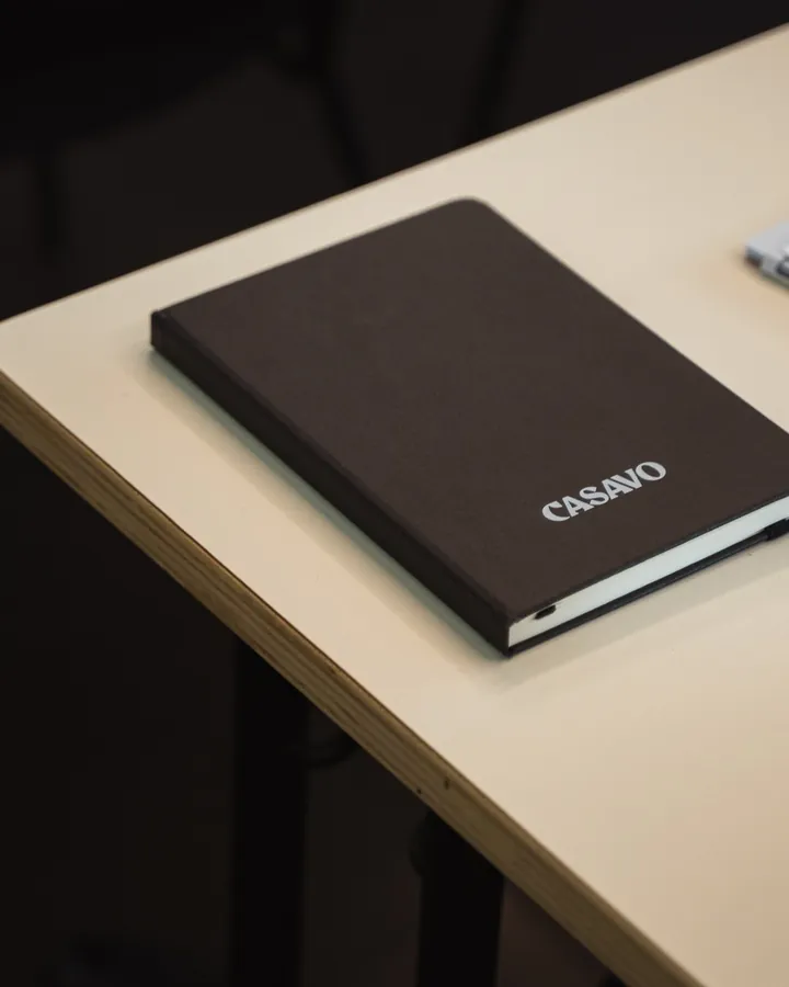 Un quaderno nero con il logo Casavo su un banco dell'aula.